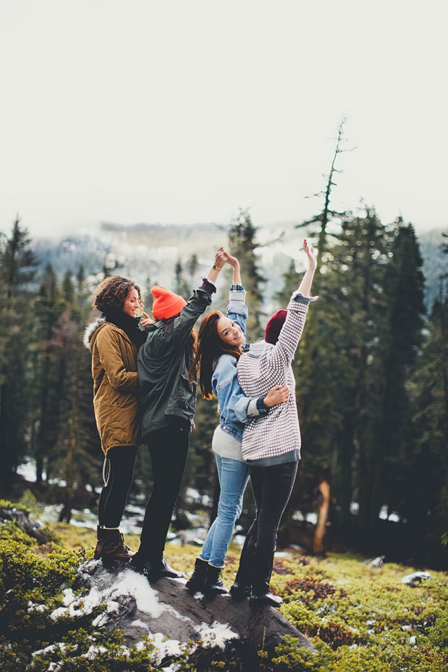 outdoor image of a group of 4 friends looking out toward nature, dressed in outdooor gear, one woman has her head turnedd back towards the camera