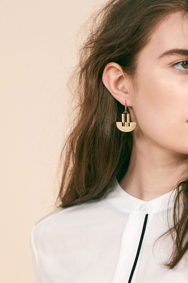 Jewellery editorial photograph of woman in white shirt looking off camera into distance wearing a dinstinct gold-earring