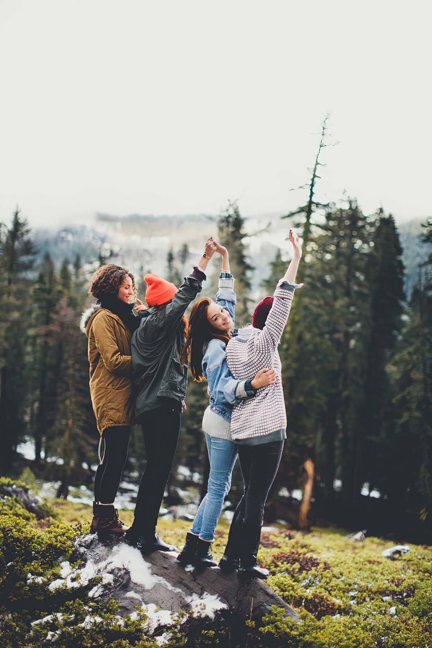 outdoor image of a group of 4 friends looking out toward nature, dressed in outdooor gear, one woman has her head turnedd back towards the camera