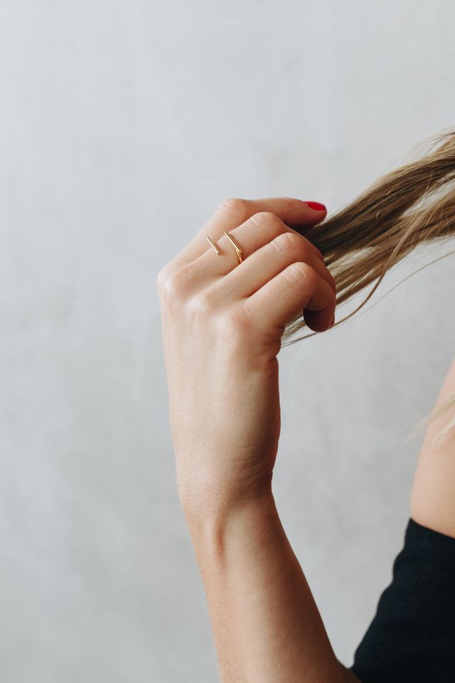 Jewellery editorial image of model's hand pulling strands of hair while camera focused on minimal gold ring on her middle finger